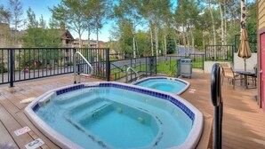 Eine Terrasse mit zwei Whirlpools, einem Pool und einem von Bäumen umgebenen, eingezäunten Bereich.