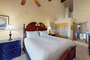 A bedroom with a large bed, wooden headboard, bedside tables with lamps, a dresser, and a door leading to another room. - La Casa #14 condo with valley views from the balcony and on-site hot tubs (Steamboat Springs)