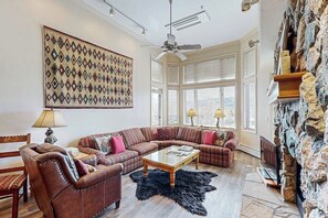 A living room with a large sofa, a coffee table, and a stone wall. - Comfortable Condo w/ Shared Pool, Gym, Hot Tub, Winter Shuttle, & Ski Lockers (Steamboat Springs)