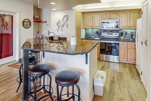 A kitchen with wooden cabinets, a stainless steel oven, a microwave, and a granite island with stools. - Comfortable Condo w/ Shared Pool, Gym, Hot Tub, Winter Shuttle, & Ski Lockers (Steamboat Springs)