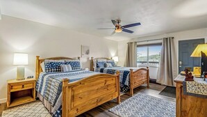 A bedroom with two wooden beds, a ceiling fan, bedside lamps, a patterned rug, and a view of the outdoors. - Lovely Lakefront Condo with  Fireplace, Free High-Speed WiFi and Stunning Views (Dillon)