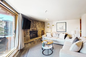 A living room with a stone fireplace, a sofa, a coffee table, and a TV mounted on the wall. - Waterfront condo with full kitchen & wifi - convenient location (Dillon)