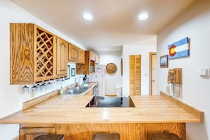 A kitchen with wooden cabinets, a central island, and a wall-mounted phone. - Comfy condo with furnished patio, & wood-burning fireplace (Silverthorne)