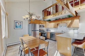 A modern kitchen with wooden cabinets, a central island, and a dining area with a wooden table and chairs. - Top-floor condo with mountain views, easy skiing, balcony & hiking (Silverthorne)