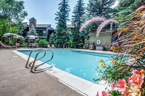 Ein Pool mit Liegestühlen und Sonnenschirmen, umgeben von Bäumen und einem Gebäude mit Schornstein.