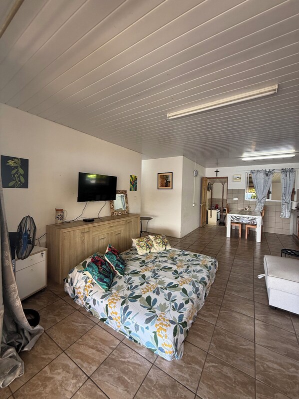 Une chambre à coucher comprenant un lit, un téléviseur, une commode en bois et un coin repas avec une table et des chaises.