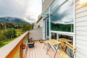 Ein Balkon mit Holztisch und -stühlen, einem Blumentopf und Blick auf eine gebirgige Landschaft.