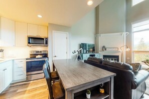 Eine moderne Küche mit eingebauten Geräten, ein Essbereich mit Holztisch und -stühlen sowie ein Wohnzimmer mit Kamin.
