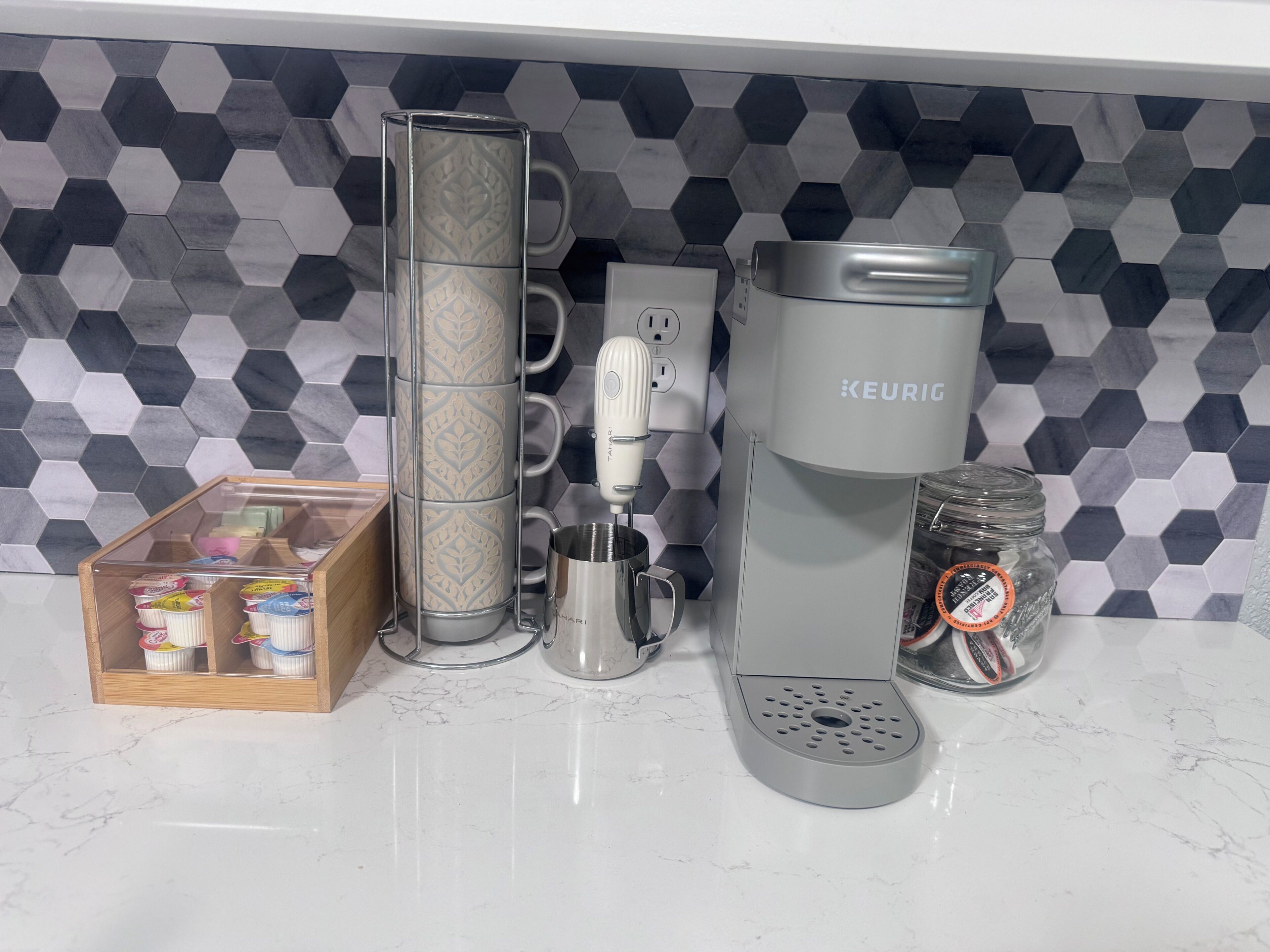 A kitchen with a coffee maker, a coffee grinder, a jar, and a container of coffee pods.