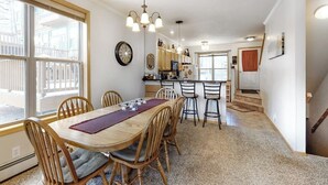 A dining area with a wooden table and chairs, a chandelier, and a view of the outside. - Inviting townhome with private hot tub, gas fireplace & deck - near skiing (Silverthorne)