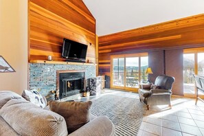 Ein Wohnzimmer mit Kamin, Wandfernseher, einer Couch und einem Sessel.