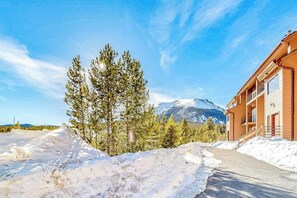 Ein Gebäude mit Holzfassade und verschneiter Landschaft, Bäume und Berge im Hintergrund.