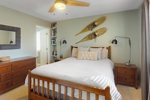 Ein Schlafzimmer mit Bett, Holz-Kopfbrett, Nachttischen, Deckenventilator, Bücherregal und Spiegel.