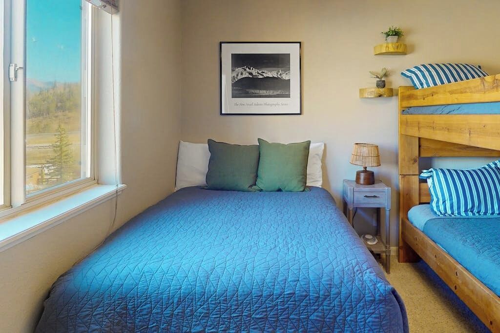 A bedroom with a bed, a nightstand, a lamp, a bunk bed, and a framed photograph on the wall.