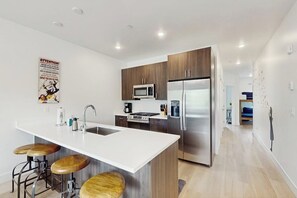 A modern kitchen with a central island, stainless steel appliances, and wooden bar stools. - Cozy condo w/ full kitchen, fast wifi, balcony & convenient location (Silverthorne)