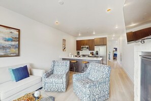 A modern living room with a white sofa, patterned armchairs, a coffee table, and a kitchen in the background. - Cozy condo w/ full kitchen, fast wifi, balcony & convenient location (Silverthorne)