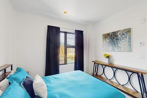 A bedroom with a bed, a window with curtains, a bedside table with a vase, and a painting on the wall. - Cozy condo w/ full kitchen, fast wifi, balcony & convenient location (Silverthorne)