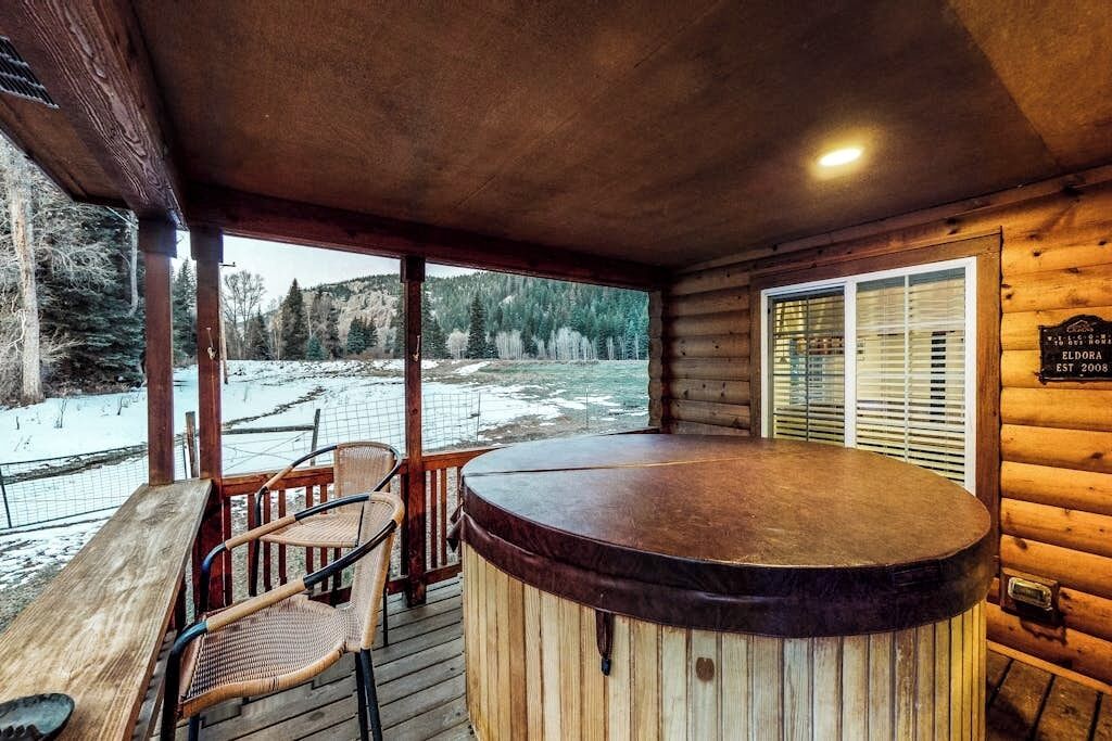 Una cabaña de madera con jacuzzi, terraza de madera y vista a un paisaje nevado.