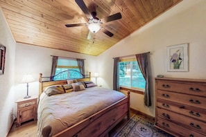 Ein Schlafzimmer mit Holzbalkendecke, einem Bett, einem Schminktisch und einem Fenster mit Vorhängen.