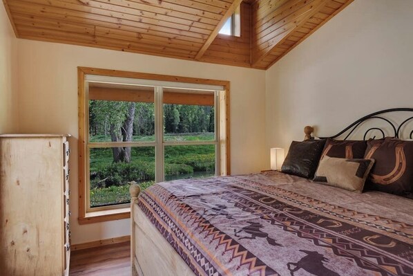 Un dormitorio con un ventanal grande, una cama con ropa de cama estampada, un cabecero de madera y una mesita de noche.