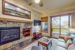Ein Wohnzimmer mit Kamin aus Stein, einem Fernseher, einer Couch und einem großen Fenster mit Blick.
