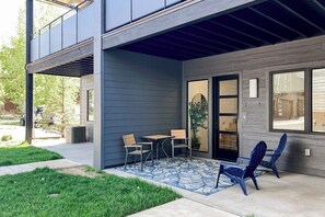 A modern two-story building with a covered patio area featuring a table and chairs, a small garden, and a visible garage. - Newly built home with pool, hot tub, & gym - walk to gondola (Steamboat Springs)