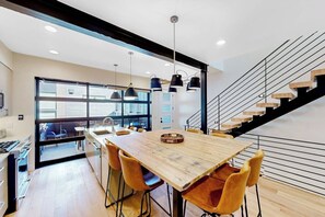 A modern kitchen with a wooden table and chairs, a staircase, and a large window. - Newly built home with pool, hot tub, & gym - walk to gondola (Steamboat Springs)