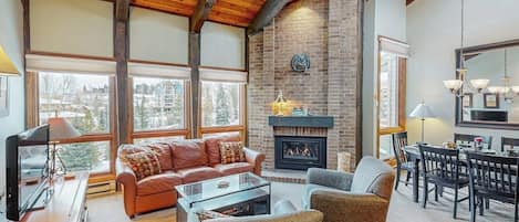 Un amplio salón con chimenea, un sofá de cuero y un comedor con candelabro.