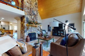 A spacious living area with a stone fireplace, leather furniture, and a high ceiling.