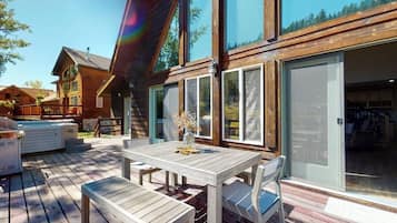 Une terrasse en bois avec une table et des chaises, un jacuzzi et une grande porte-fenêtre coulissante.