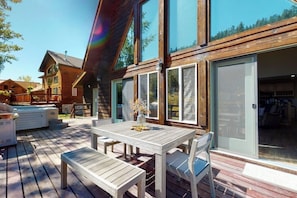 Une terrasse en bois avec une table et des chaises, un jacuzzi et une grande porte-fenêtre coulissante.