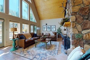 A spacious living room with a stone fireplace, large windows, and a cozy seating area.