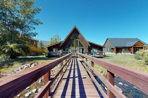 A wooden bridge leading to a lodge with a triangular roof and a second building with a similar roof style.