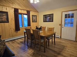 Ein Essbereich mit Holztisch und Stühlen, einer Tür mit Fenster und gerahmten Bildern an den Wänden.