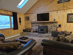 Ein gemütliches Wohnzimmer mit Kamin aus Stein, Ledersofas, einem Flachbildfernseher und einer Holzbalkendecke.