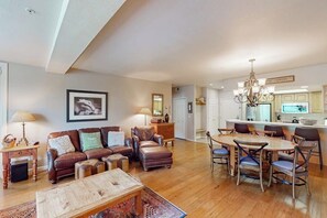 Ein großzügiges Wohnzimmer mit Sofa, Hocker und Couchtisch, ein Essbereich mit Holztisch und Stühlen sowie eine Küche mit einer Deckenleuchte.