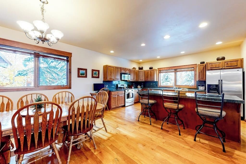 A kitchen with wooden cabinets, a dining table with chairs, and a large window.