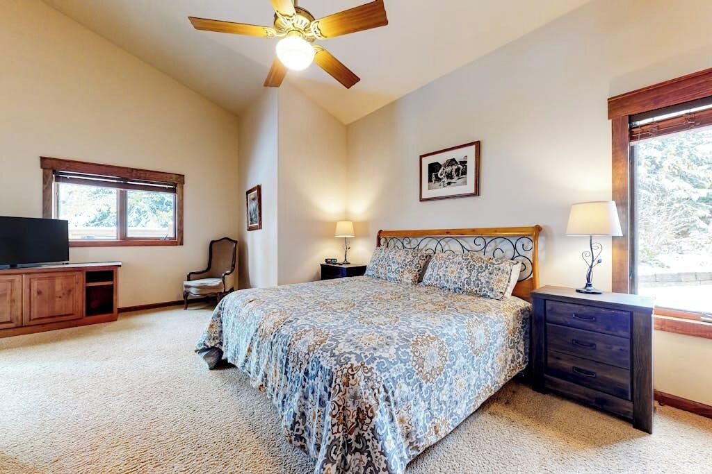 A bedroom with a bed, a ceiling fan, a television, a window, and a nightstand.