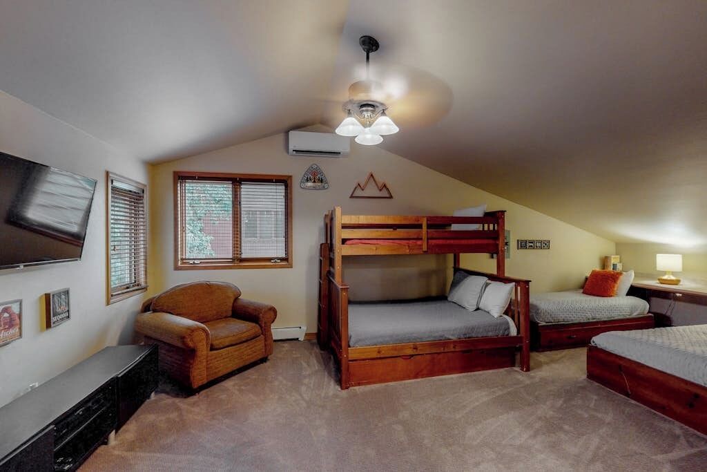 A dormitory room with bunk beds, a television, a chair, and a ceiling fan.