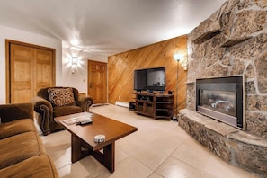 Ein Wohnzimmer mit Kamin aus Stein, Holzwänden, einem Fernseher und einer Couch.