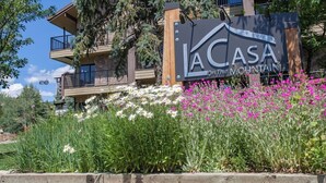 Un edificio de varios pisos con balcones, un cartel que dice 'LA CASA on The Mountain' y una variedad de flores en la fachada.