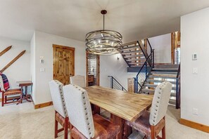 A dining area with a wooden table and chairs, a hanging light fixture, a staircase, and a wooden door. - Upscale Ski Condo w/ WiFi, Guest Fireplaces, 2 Shared Hot Tubs, & Partial AC (Steamboat Springs)