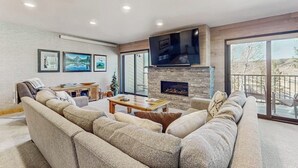 Una sala de estar moderna con un sofá modular, un televisor de pantalla plana, chimenea y ventanas amplias.