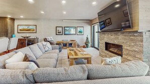 Una sala de estar con un sofá modular, una chimenea, un televisor de pantalla plana y cuadros en la pared.