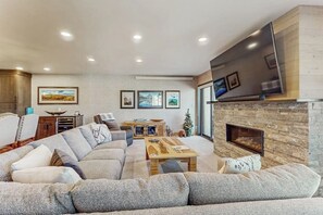 A living room with a sectional sofa, a fireplace, a flat-screen TV, and framed artwork on the wall. - Upscale Ski Condo w/ WiFi, Guest Fireplaces, 2 Shared Hot Tubs, & Partial AC (Steamboat Springs)