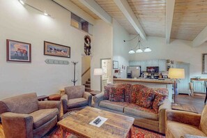 A spacious living room with sofas, a coffee table, and a kitchen in the background. - Charming condo next to the gondola with high-speed WiFi, hot tub & pool (Steamboat Springs)