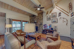 A cozy living room with a stone wall, wooden ceiling, and a fireplace. There are leather sofas, a coffee table, and a TV. - Charming condo next to the gondola with high-speed WiFi, hot tub & pool (Steamboat Springs)