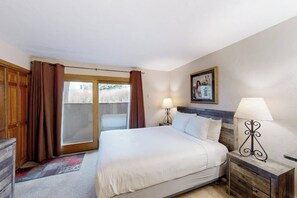 Ein Schlafzimmer mit einem Bett, zwei Nachttischlampen, einem hölzernen Kopfteil, einem Fenster mit Vorhängen und einem gerahmten Bild an der Wand.