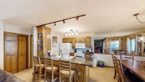 Une cuisine avec des meubles en bois, un îlot central doté de tabourets, une table à manger avec des chaises et des luminaires suspendus.