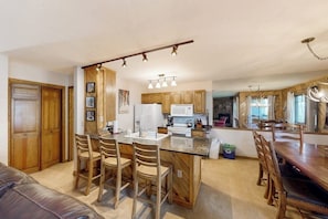 A kitchen with wooden cabinets, a central island with bar stools, a dining table with chairs, and pendant lighting. - Ground-floor home with high-speed WiFi, pool & hot tub - next to lift (Steamboat Springs)